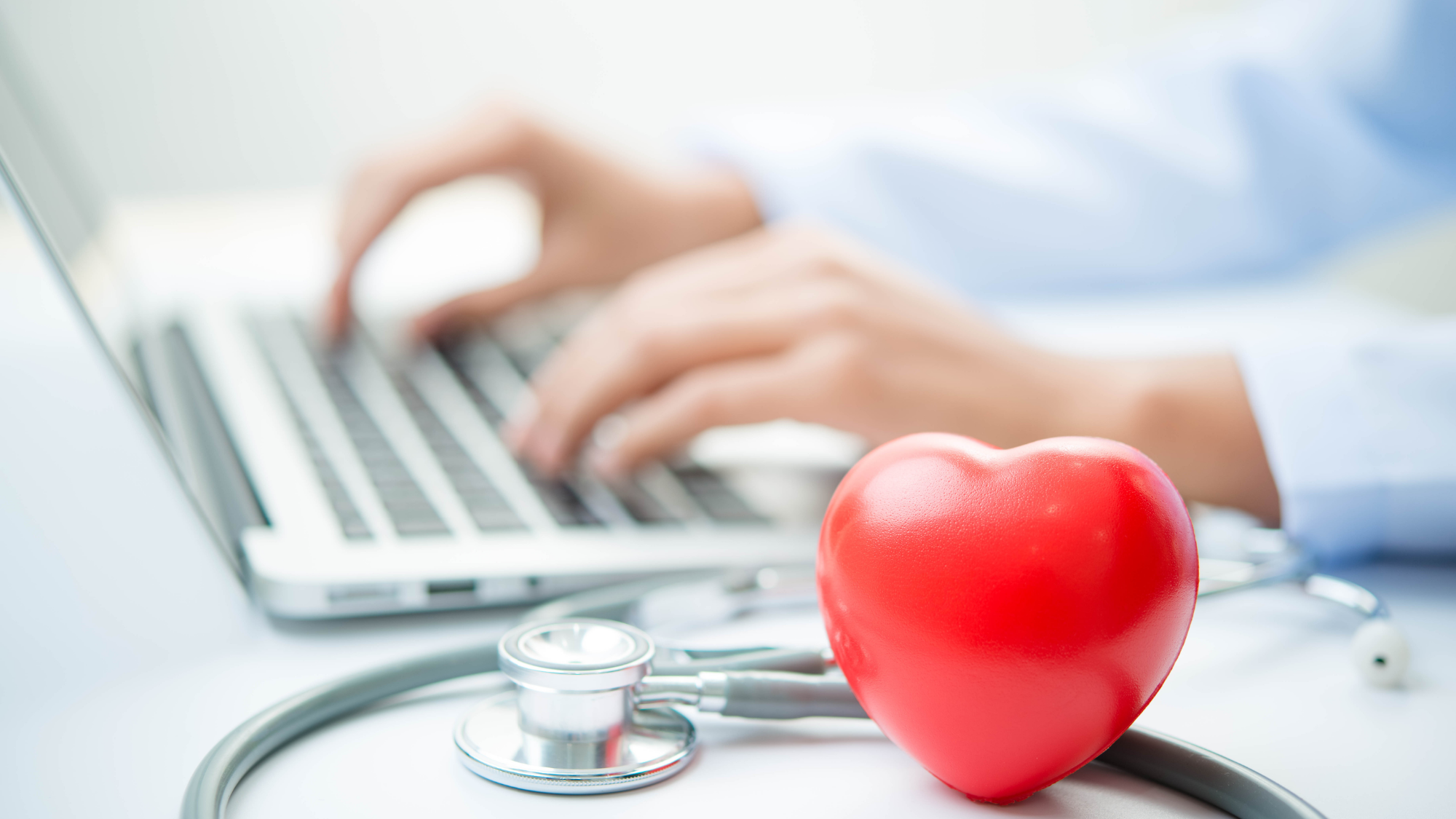 heart and a stethoscope, blurry background with hands on laptop
